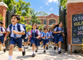स्कूली बच्चे छुट्टी के बाद खुशी से बैग लेकर बाहर भागते हुए और पृष्ठभूमि में School Holiday 2026 लिखा बोर्ड
